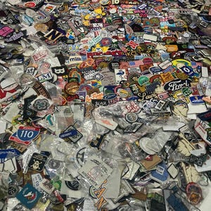 Könnte beinhalten: Eine große Sammlung verschiedener bestickter Stoffaufnäher in unterschiedlichen Formen, Farben und Designs, von denen viele einzeln in durchsichtigen Plastiktüten verpackt sind. Die Aufnäher zeigen diverse Logos, Texte, Symbole und Illustrationen.