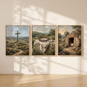 May include: Set of three framed art prints. The first depicts a wooden cross on a hill. The second shows a crown of thorns on a stone. The third shows an empty tomb with a large stone rolled away. The art has a soft, painterly style.