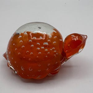 Puede incluir: Una pequeña figura de tortuga de vidrio naranja con una concha de vidrio transparente. La concha está cubierta de pequeñas burbujas blancas.