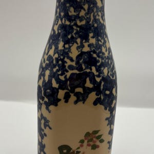 May include: A blue and white ceramic milk bottle vase with a painted scene of a person picking fruit from a tree.