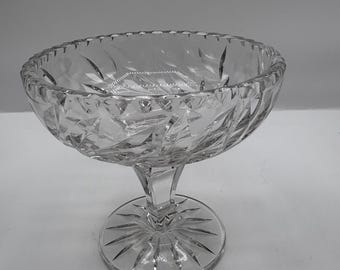 Può includere: Una coppetta da dessert in vetro trasparente tagliato, con base a piedistallo. La coppetta ha un bordo smerlato e un motivo geometrico. La base è rotonda con un disegno a stella. La coppetta misura circa 15 cm di diametro.