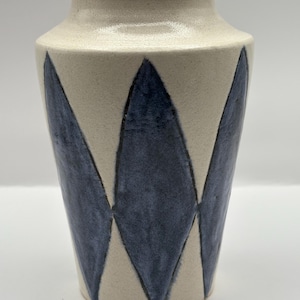 May include: A ceramic vase with a cream-colored base and navy blue diamond pattern. The vase has a wide base that tapers to a narrower neck and rim. The design is simple and modern, suitable for home decor.
