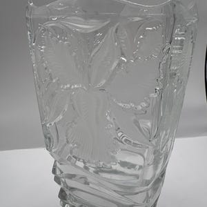 May include: Clear glass vase with a floral pattern. The vase has a rectangular shape with a flared top and a textured, ridged base. The floral design is etched into the glass, creating a frosted effect.