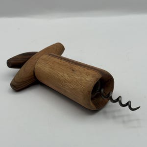 May include: A wooden corkscrew with a dark brown handle and a light brown barrel. The metal worm is visible at the end of the barrel. The corkscrew is designed for removing corks from wine bottles.