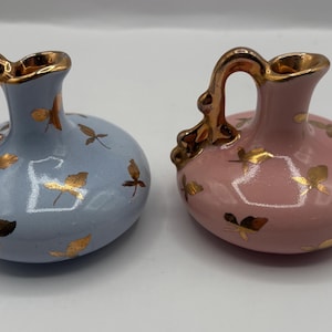 May include: Two small ceramic pitchers with gold leaf accents. One pitcher is light blue and the other is pink.