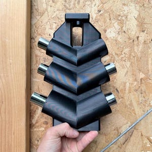 May include: A black, chevron-patterned tool holder featuring six cylindrical silver metal ports arranged in three pairs along the sides. The structure is made of a dark, textured material with a rectangular opening at the top centre for mounting.