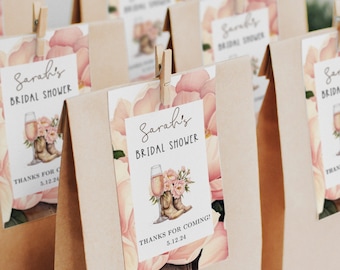 May include: A set of brown paper favor bags with pink floral and cowboy boot themed labels. The labels say "Sarah's Bridal Shower" and "Thanks for coming! 5.12.24".