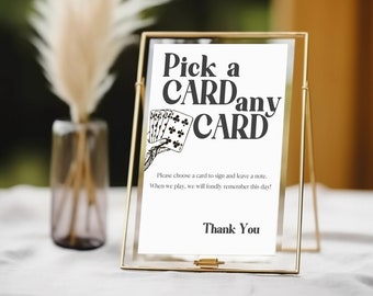 Può includere: Un cartello con cornice dorata con il testo "Pick a CARDany CARD" e un'illustrazione in bianco e nero di carte da gioco. Il cartello include anche il testo "Per favore, scegli una carta per firmare e lascia un biglietto. Quando giocheremo, ricorderemo con affetto questo giorno! Grazie."