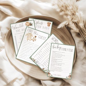 May include: A collection of baby shower game cards with various designs and text. The cards include games like "Would She Rather" and "Baby Family Feud." The cards are white with green borders and decorative floral elements.