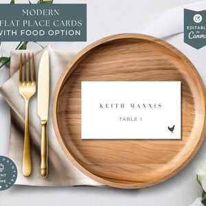 May include: A white place card with the text "Keith Mannis" and "Table 1" printed in black. A small black chicken icon is in the bottom right corner of the card. The card is on a wooden plate.