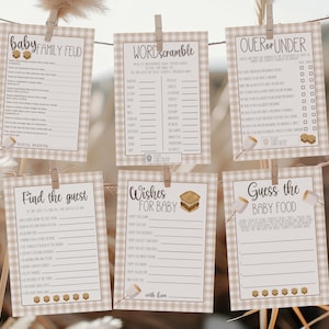 May include: Six printable baby shower games, including "Baby Family Feud" and "Guess the Baby Food", are displayed. Each game card has a tan and white gingham border and is held by a wooden clothespin. The games are strung on a thin wire.
