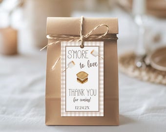 May include: A brown paper gift bag tied with twine, featuring a tag with a s'mores graphic and the text "S'more to love. Thank you for coming!" The tag has a checkered border and a watercolor illustration of a s'more.