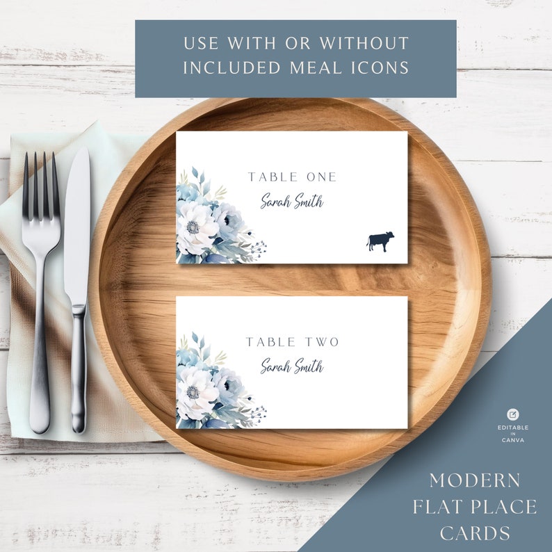 May include: Two white place cards with blue floral designs and the text "Table One Sarah Smith" and "Table Two Sarah Smith". The cards are on a wooden plate with a fork and knife on a white wooden surface.
