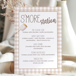 Puede incluir: Un letrero a cuadros beige y blanco con las palabras "S'MORE station" en una fuente manuscrita. El letrero enumera recetas de s'mores, incluyendo "The Classic Cutie" y "Berry Sweet Baby".