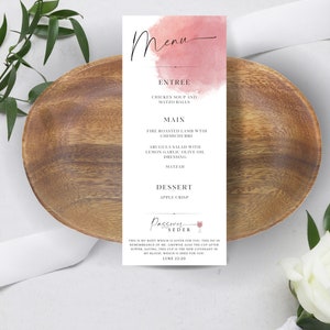 Può includere: Un menu stampabile con uno sfondo ad acquerello in tonalità rosa. Il menu presenta un pasto di Seder di Pasqua con piatti come zuppa di pollo, agnello arrosto al fuoco e torta di mele. Il testo "Passover Seder" è scritto in corsivo con un'icona di bicchiere di vino.