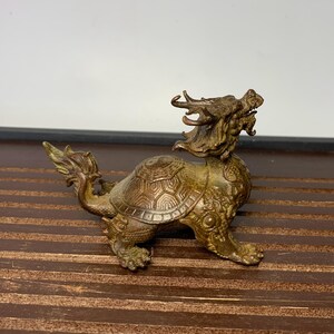 May include: A bronze sculpture of a dragon turtle, a mythical creature with the head of a dragon and the body of a turtle. The sculpture is detailed with intricate carvings and has a weathered patina.
