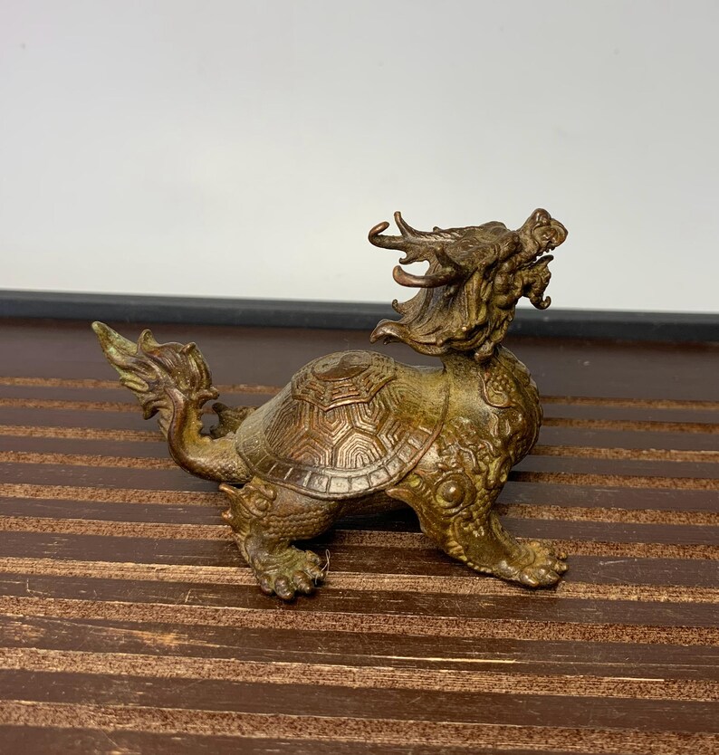 May include: A bronze sculpture of a dragon turtle, a mythical creature with the head of a dragon and the body of a turtle. The sculpture is detailed with intricate carvings and has a weathered patina.