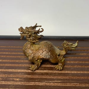May include: A bronze sculpture of a dragon and turtle, a mythical creature in Chinese culture. The dragon is depicted with a long, serpentine body and a fierce expression, while the turtle is shown with a hard shell and four legs. The sculpture is a traditional Chinese art form and is often used as a symbol of good luck and prosperity.