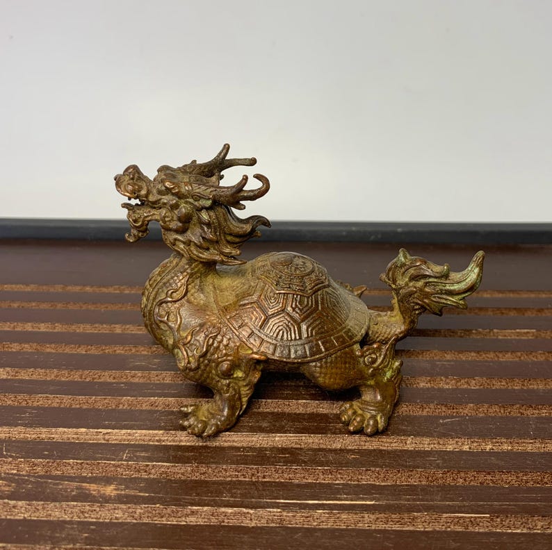 May include: A bronze sculpture of a dragon and turtle, a mythical creature in Chinese culture. The dragon is depicted with a long, serpentine body and a fierce expression, while the turtle is shown with a hard shell and four legs. The sculpture is a traditional Chinese art form and is often used as a symbol of good luck and prosperity.