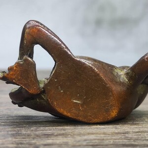 May include: A bronze frog figurine in a relaxed pose, with its legs extended. The frog is lying on its back, with its arms and legs in the air. The figurine has a smooth, polished surface and is a warm brown color.