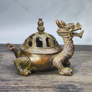 May include: Bronze incense burner in the shape of a turtle with a dragon head. The turtle's shell has a decorative, openwork design. The burner has a small, ornate finial on top. The overall design is detailed and antique-looking.