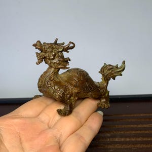 May include: A bronze sculpture of a dragon turtle, a mythical creature with the head of a dragon and the body of a turtle. The sculpture is intricately detailed and has a weathered patina.
