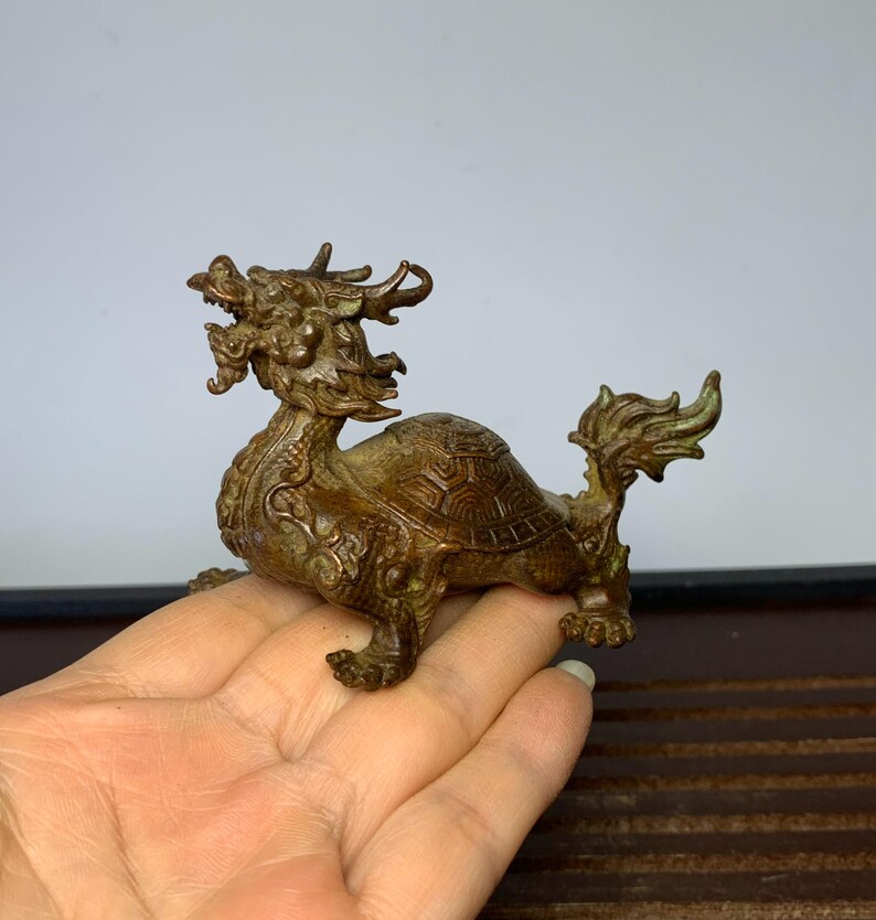 May include: A bronze sculpture of a dragon turtle, a mythical creature with the head of a dragon and the body of a turtle. The sculpture is intricately detailed and has a weathered patina.