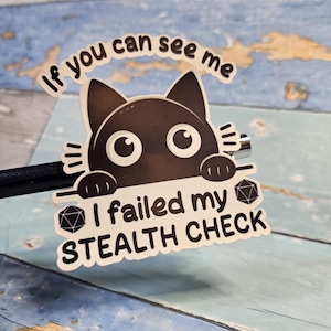 May include: A black cat peeking over a white sticker with the text "If you can see me I failed my stealth check" and a black and white dice graphic.