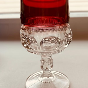 May include: A clear glass goblet with a red glass top. The goblet has a round base and a stem with a decorative design. The goblet is ideal for serving wine or other beverages.