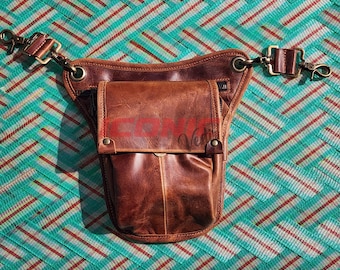 Könnte beinhalten: Eine braune Hüfttasche aus Leder mit Klappenverschluss und verstellbaren Riemen. Die Tasche hat eine Vordertasche und ist mit messingfarbener Hardware versehen. Die Tasche befindet sich vor einem türkis-roten Hintergrund.