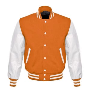Op de afbeelding: Oranje en witte varsity jas met een knoopsluiting. De jas heeft witte mouwen, een zwarte kraag en witte strepen op de manchetten en zoom. Een klassieke stijl van bovenkleding.