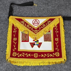 May include: A red and white masonic apron featuring gold fringe trim, embroidered floral vines, and two red tabs with gold chains. The center displays a multi-colored square grid emblem above two red triangles, with a white flap bearing a red circle symbol.