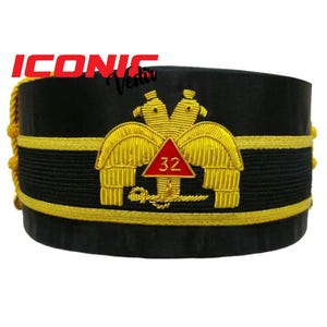 Puede incluir: Sombrero masónico negro y dorado con un emblema rojo y dorado que representa dos águilas y el número 32.