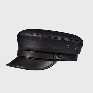 Puede incluir: Gorra de capitán de cuero negro con una visera corta y un detalle de correa. El sombrero presenta una corona estructurada y un cierre de botón en el lateral. El sombrero tiene dos pequeños ojales metálicos en el lateral.