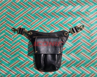 May include: Black leather hip bag with a flap and two front pockets. The bag has a red text that says "ICON". The bag has adjustable straps with gold-colored metal clasps. The background is a teal, red, and white patterned fabric.