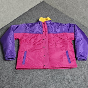 Puede incluir: Chaqueta colorida de estilo retro. La parte superior es morada, el centro rosa brillante y el cuello amarillo. La chaqueta tiene una botonadura frontal y dos bolsillos. Las mangas y los puños son morados.