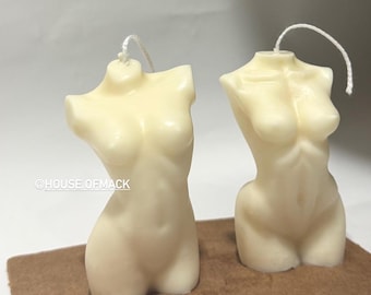 Peut inclure: Deux bougies blanc cassé en forme de torse, chacune surmontée d'une mèche blanche. La bougie de gauche porte l'inscription @HOUSE OF MACK en blanc sur le côté. Les deux bougies sont sculptées pour représenter une forme de buste humain.