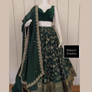May include: A dark green, three-piece formal outfit. The set includes a velvet crop top, a long skirt with a floral pattern, and a matching scarf. The skirt and scarf have gold trim. The text "Febull Studio" is in a black box.
