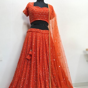 Könnte beinhalten: Ein leuchtend oranges indisches Brautkleid mit einem paillettenbesetzten Rock, einem passenden Oberteil und einem durchsichtigen orangefarbenen Dupatta mit goldenen Verzierungen.