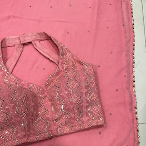 以下が含まれることがあります： 幾何学模様のピンクのノースリーブブラウス。バックスタイルはキーホールネックになっており、小さなスパンコールとビーズで飾られています。