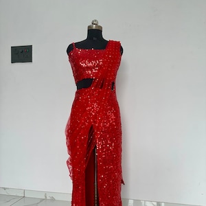 May include: A striking red sequined dress on a mannequin. The dress has a square neckline, a cutout, and a high slit. The fabric is covered in shimmering sequins, creating a glamorous effect. The dress is suitable for formal occasions.