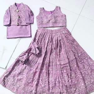 以下が含まれることがあります： 薄紫色の女の子用の衣装。刺繍入りのノースリーブトップ、刺繍入りのロングスカート、それに合わせたジャケット。特別な機会に最適な衣装です。