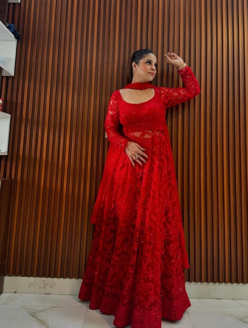 May include: A vibrant red, long-sleeved dress with intricate lace detailing. The dress features a scoop neckline and a flowing skirt. The outfit includes a matching scarf. The dress is suitable for special occasions.