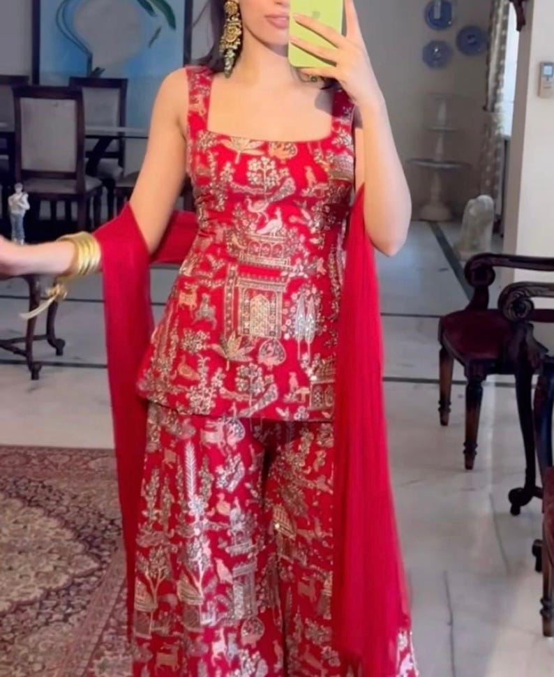 May include: A red embroidered outfit featuring a square-neck top and wide-leg pants. The outfit is adorned with gold embellishments and a matching red scarf. The ensemble is a traditional style, suitable for special occasions.