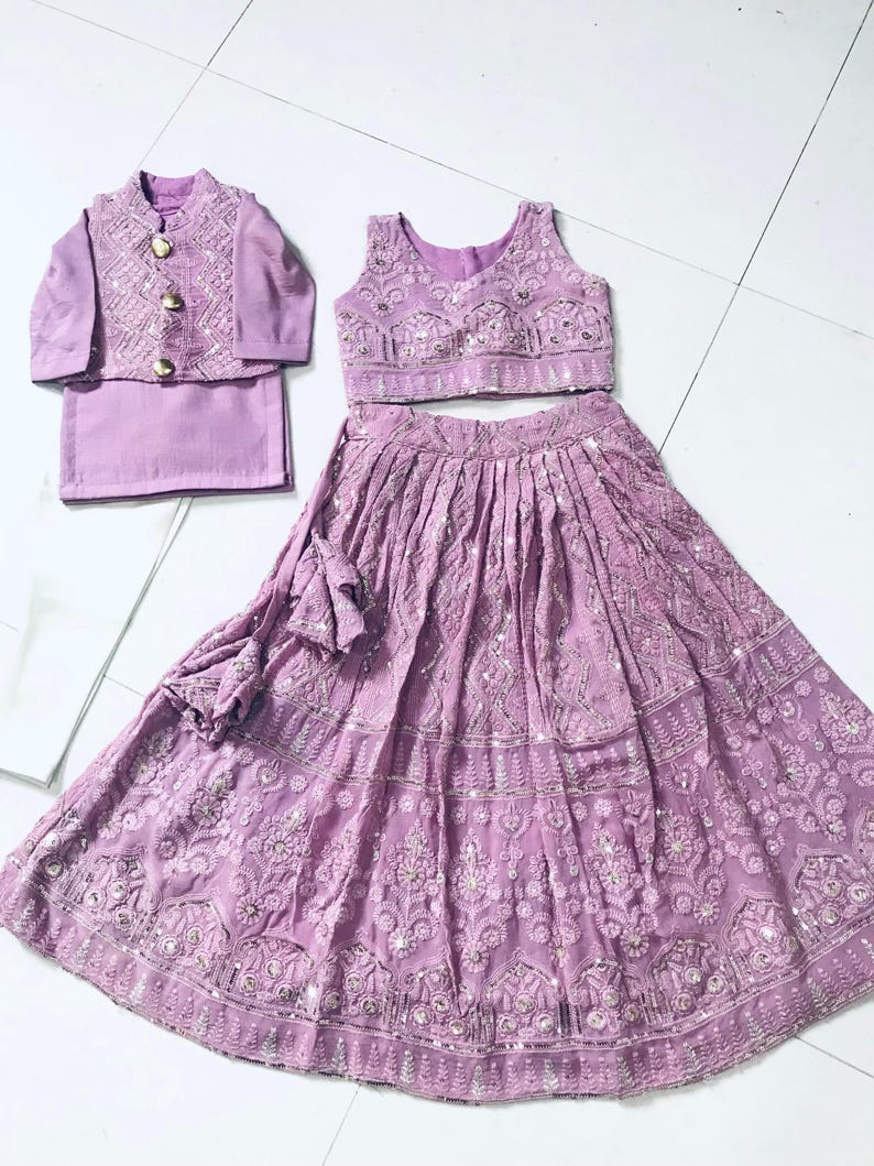 以下が含まれることがあります： 薄紫色の女の子用の衣装。刺繍入りのノースリーブトップ、刺繍模様のロングスカート、それに合わせたジャケット。特別な機会に最適な衣装です。