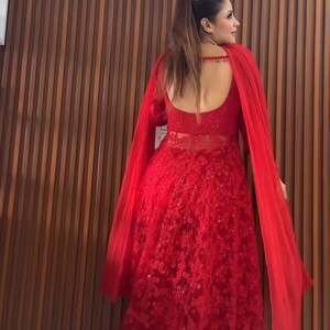 May include: A long, red, formal gown with intricate floral lace detailing. The dress features long sleeves, a low back, and a flowing cape. The gown is suitable for special occasions.