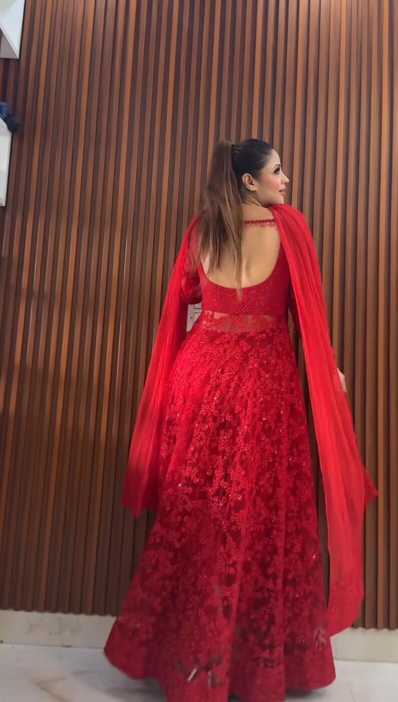 May include: A long, red, formal gown with intricate floral lace detailing. The dress features long sleeves, a low back, and a flowing cape. The gown is suitable for special occasions.