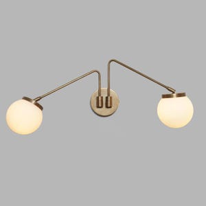 May include: A brass wall sconce with two frosted glass globes. The sconce has a modern, minimalist design.