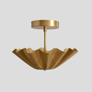 May include: A gold-colored ceiling light fixture with a ruffled, bowl-shaped shade. The fixture has a central stem and a circular base for mounting. The shade has a wavy, textured design, and the overall aesthetic is elegant and modern.