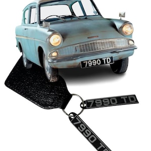 May include: A light blue vintage car with the license plate number 7990 TD. The car is accompanied by a black keychain with two tags, each displaying the same license plate number. The car's headlights are illuminated.